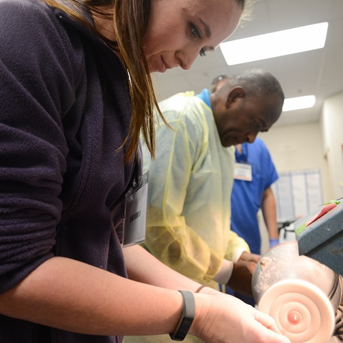 student and program director use machine to shape dentures