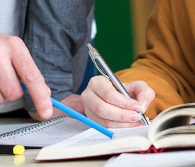 student writes in a book at tutor points to text with his pen