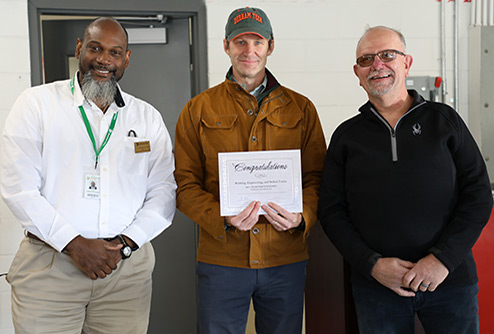 President Buxton poses with a certificate of achievement with two employees