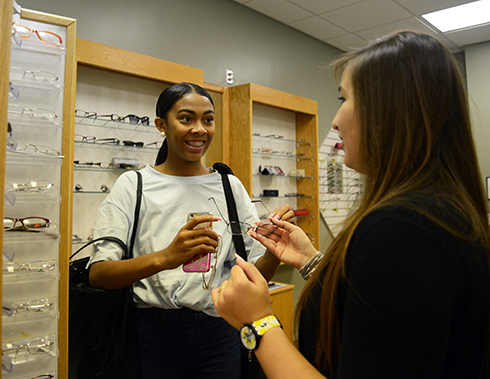 Opticianry student assists a college student in trying on glasses