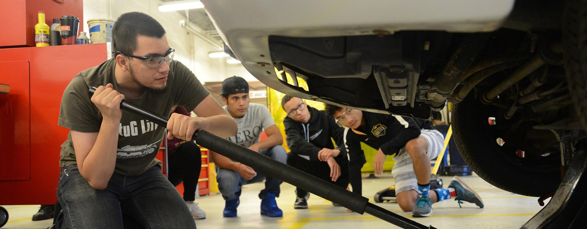 students watch a fellow student jack up a car in auto lab
