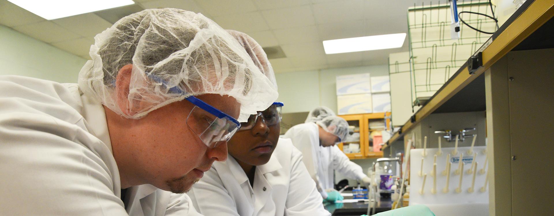 biotechnology students wearing lab coats and paper caps work in a chemistry lab