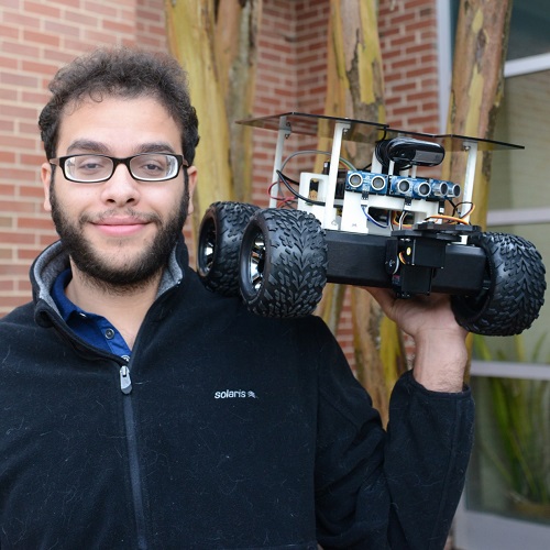 headshot of Mohamed standing in front of tree and holding up rover on his left shoulder