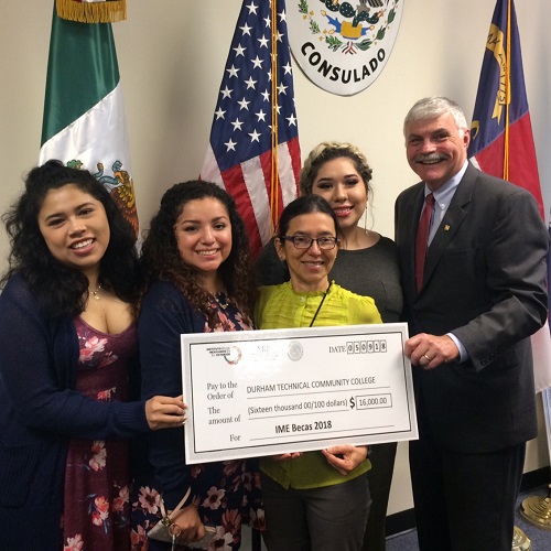 Four students and Dr. Ingram holding check in front of four flags, including Mexico's flag, American flag, North Carolina Flag and South Carolina Flag
