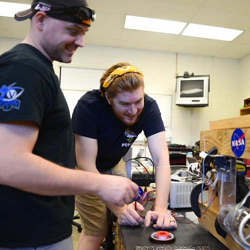 two students leaning over table looking at gadet with NASA sticker