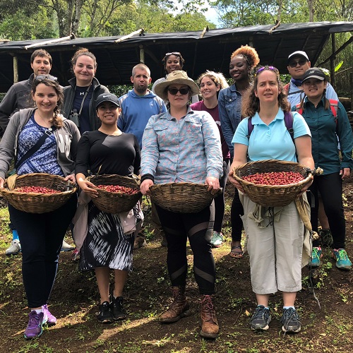 Group photo of students holding baskets of coffee beans on coffee farm