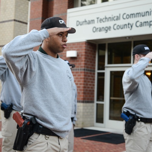 students saluting flag outside of orange county campus building
