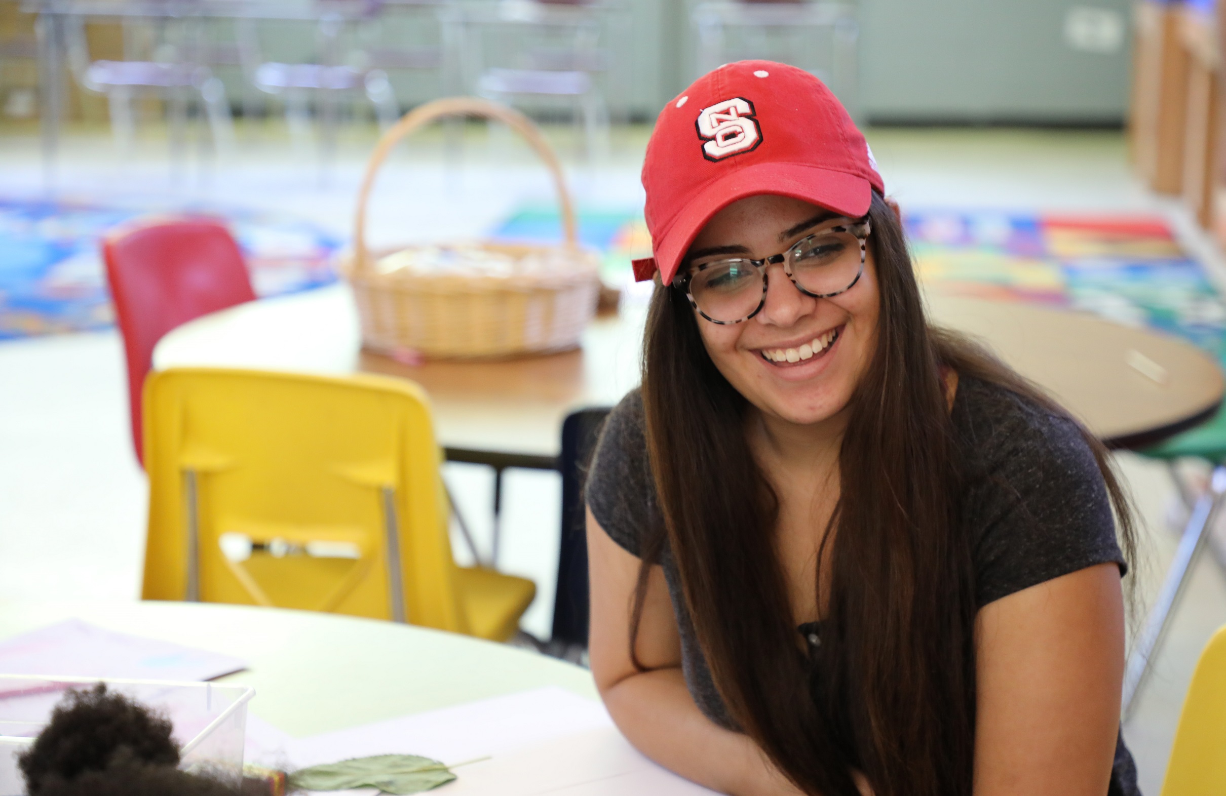 student with long hair and glasses and red hat smiling