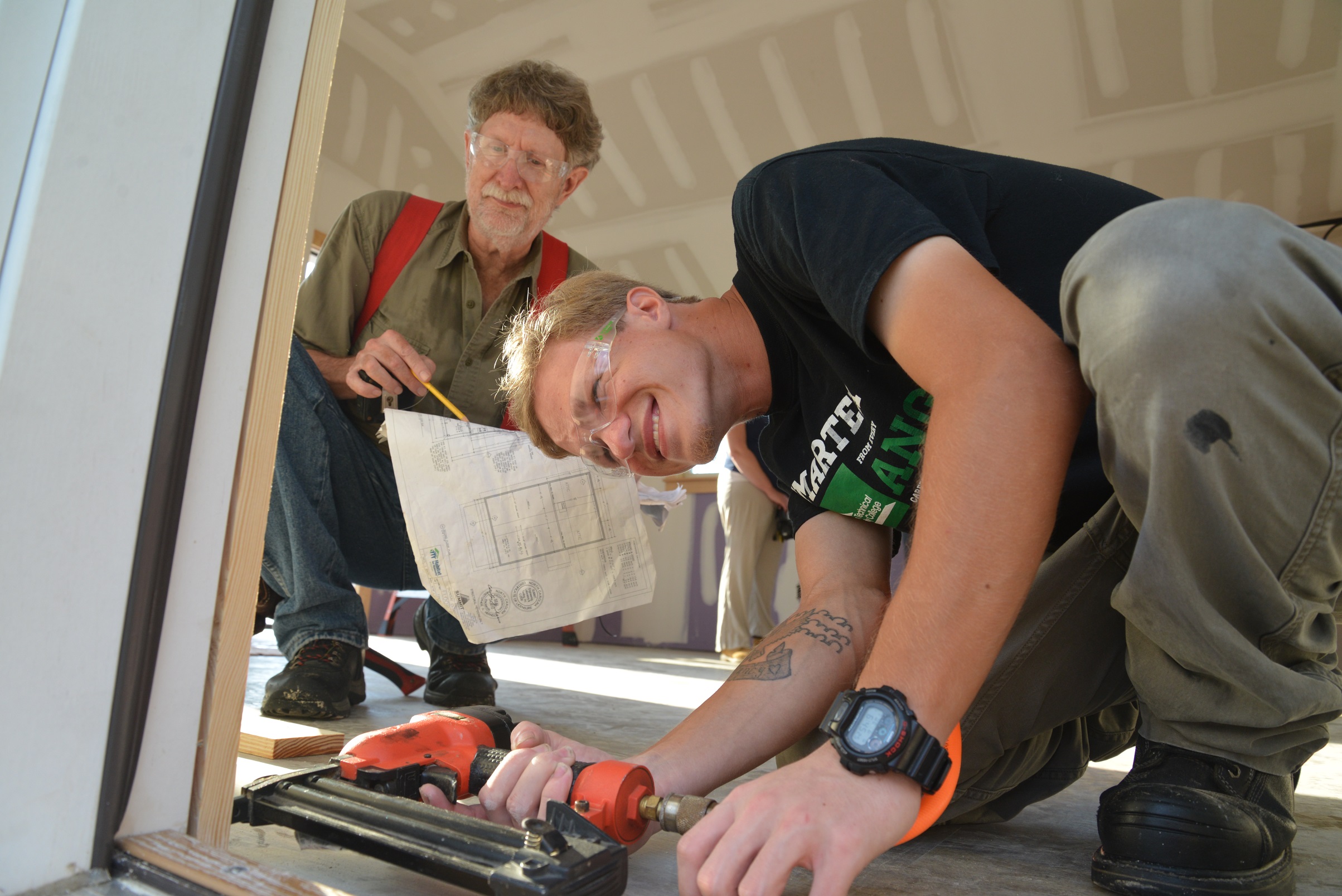 student leaning over using nail gun and another student looking over shoulder