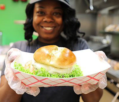 female student holding out a hamburger with metlting cheese to the camera