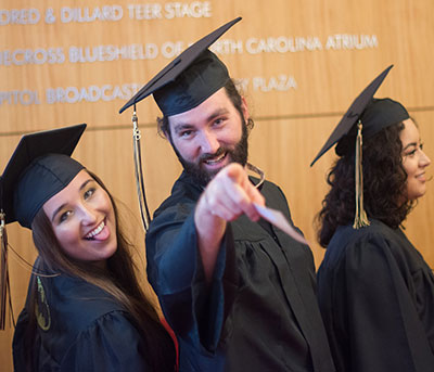male and female students in commencement regalia making funny faces and pointing at camera