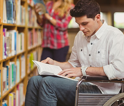 male student in wheelchair reading a book in the library