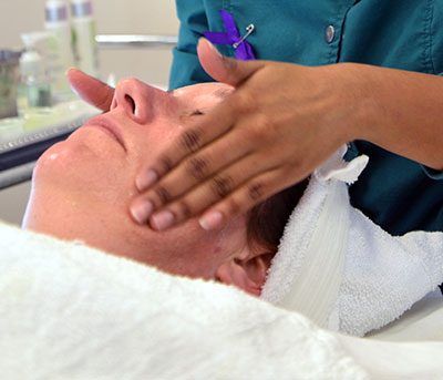 esthetics student giving a women relaxing on a table a facial massage