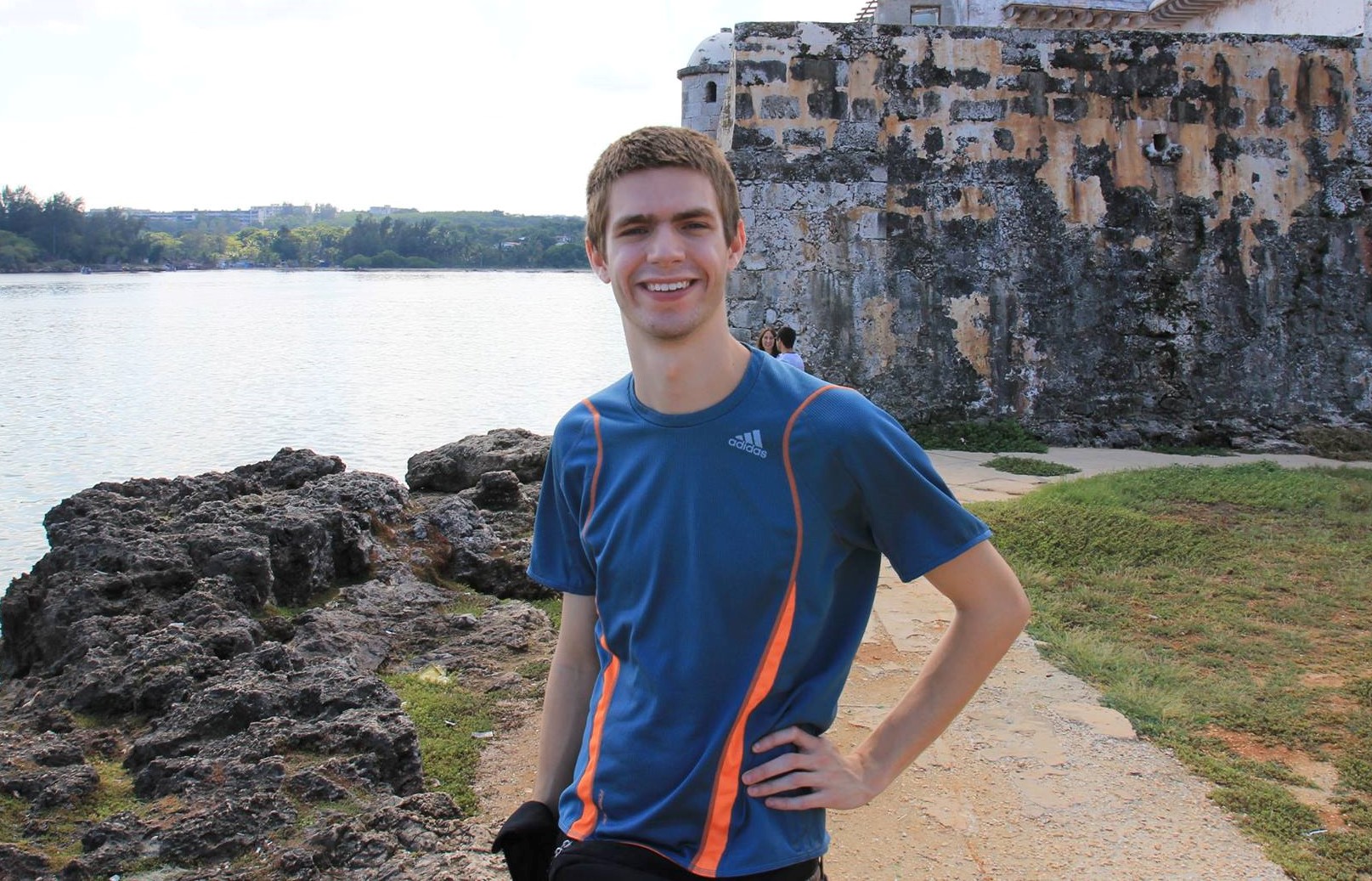 will smiling at camera with water on one side and stone building on other side in background