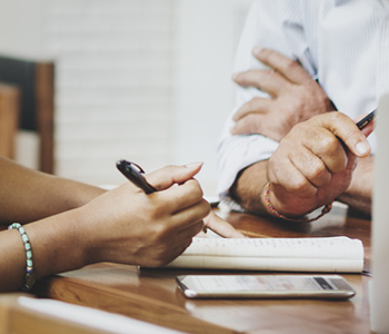 close up image of hands with two people sitting at a table talking and taking notes 