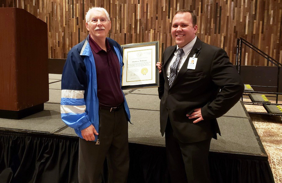 two men holding an award standing in front of a stage smiling