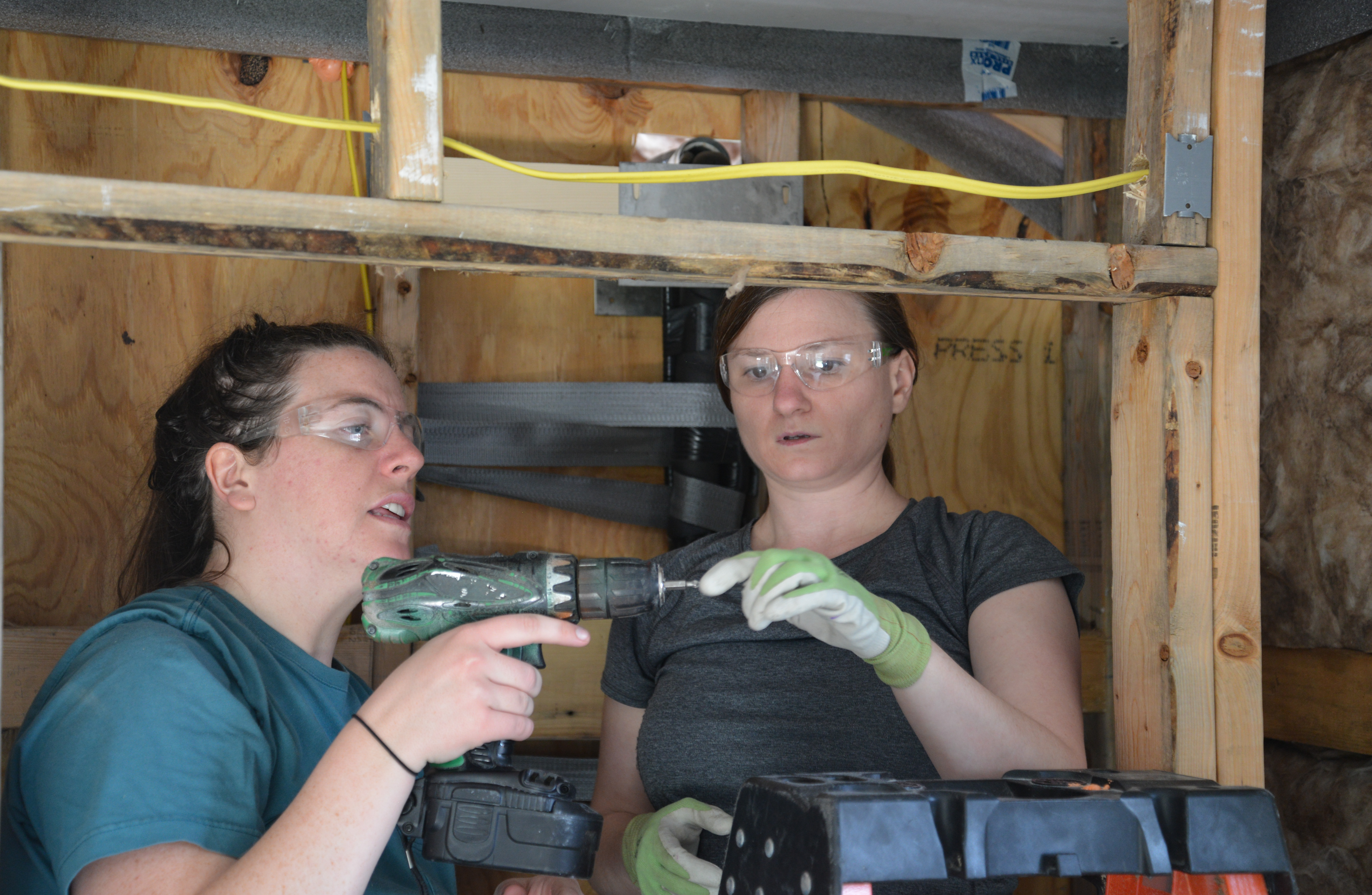 two people holding power tools working on building a house