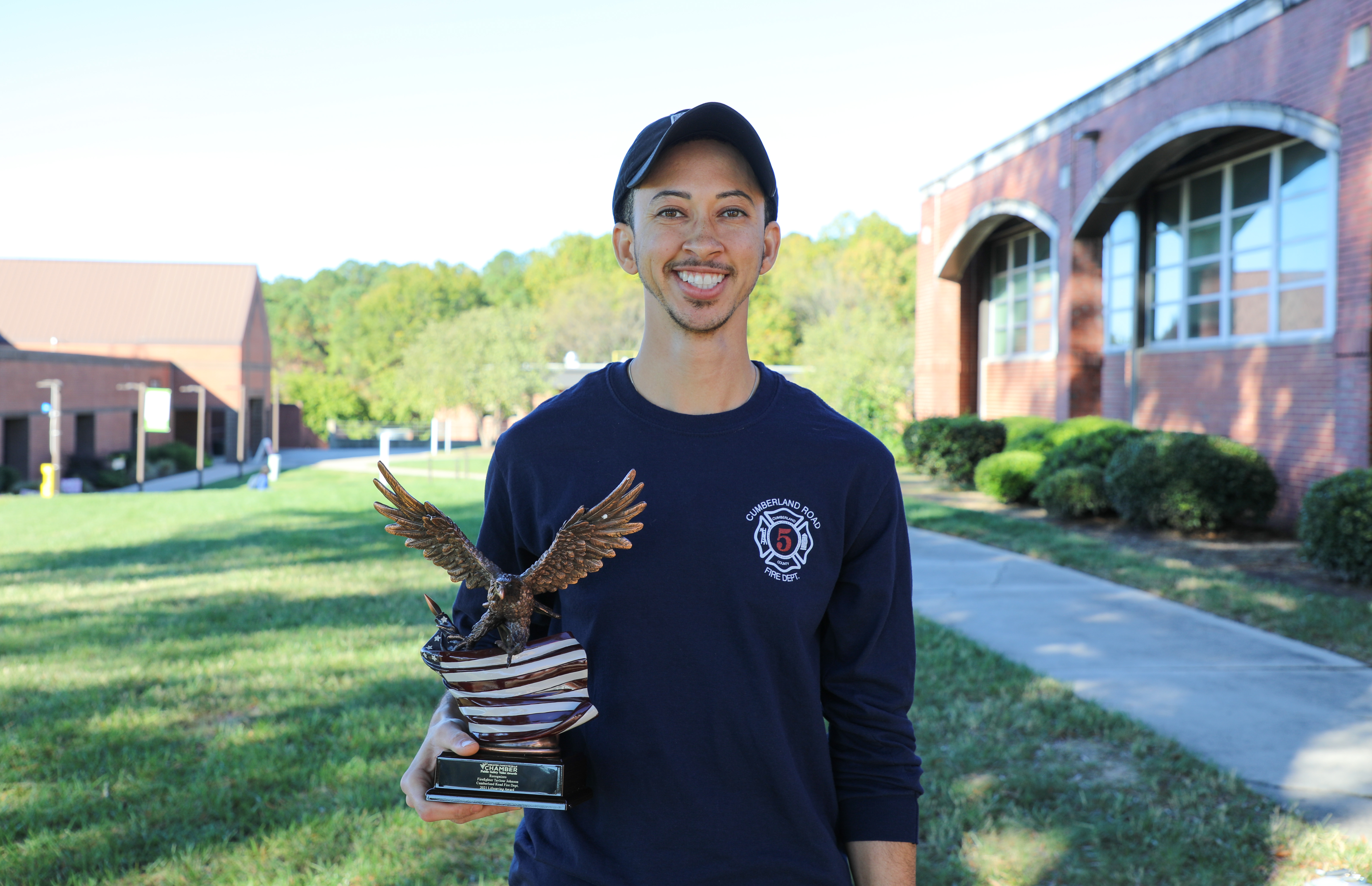 person holding eagle trophy and smiling on campus