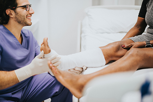 medical person in scrubs speaks with patient wearing leg cast