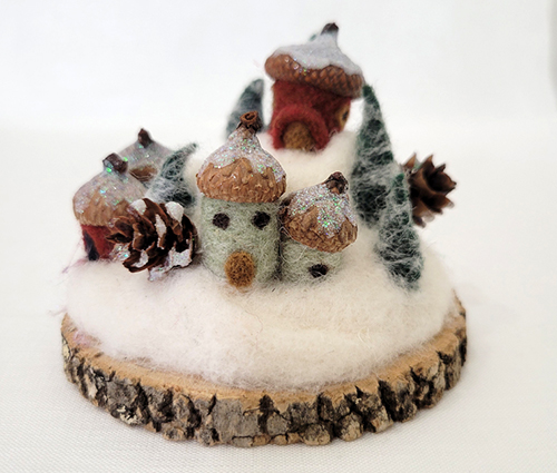 felted acorns with eyes and noses sitting on a cross section of a tree