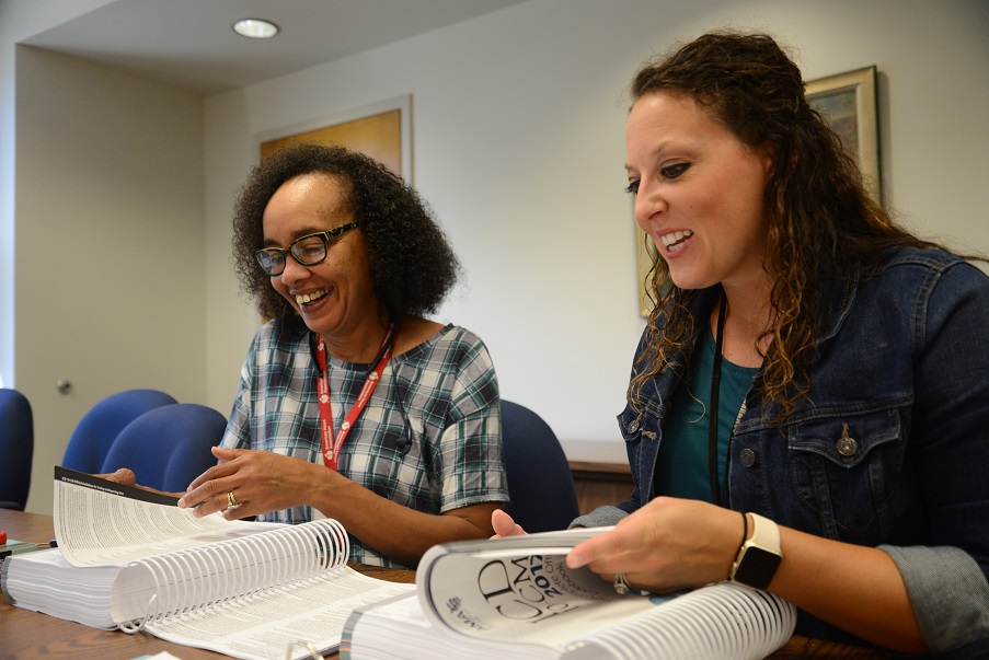 student and instructor sitting at table and smiling in front of textbooks