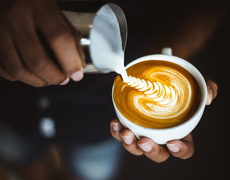 barista pouring a design into a coffee with whipped milk