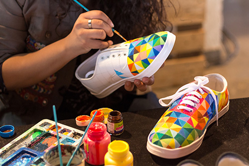 person paints a colorful design on their canvas sneakers