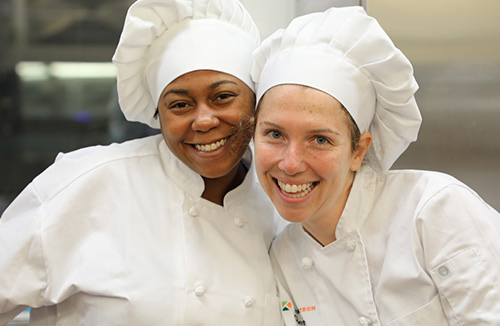 two culinary arts students in uniform smiling for the camera