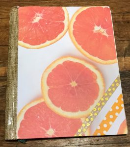 a notebook covered with paper of grapefruit slices and strips of patterned paper
