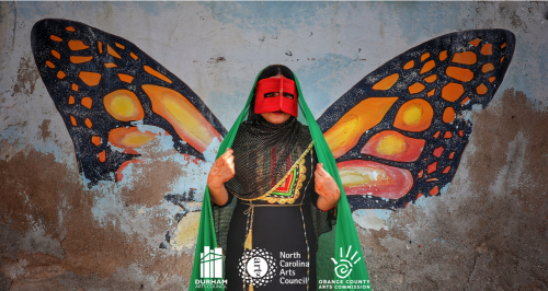 Iranian woman in traditional dress wearing an orange mask poses again a painting of butterfly wings on a wall behind her