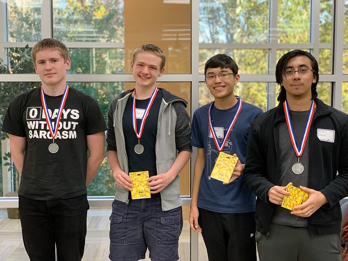 four students smiling, holding gift cards, and wearing medals around neck