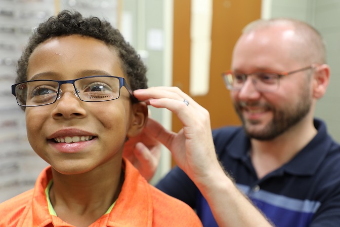 smiling child getting fitted with glasses by opticianry instructor