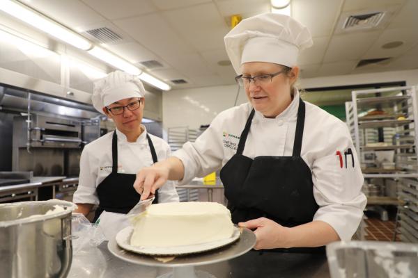 chef helping student with cake in pastry kitchen