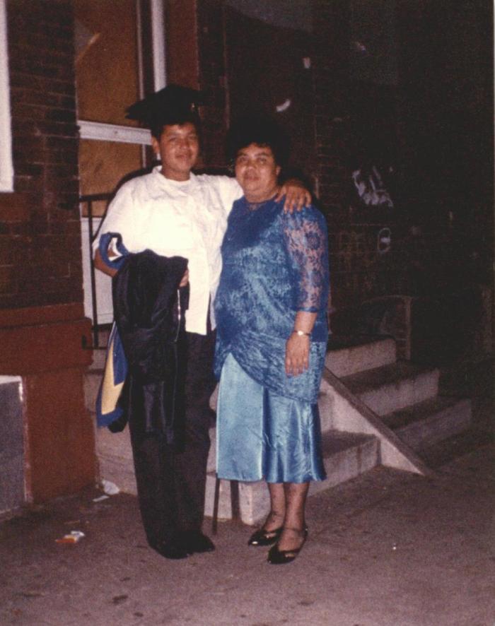 Two people standing and smiling, one has cap and gown in hand