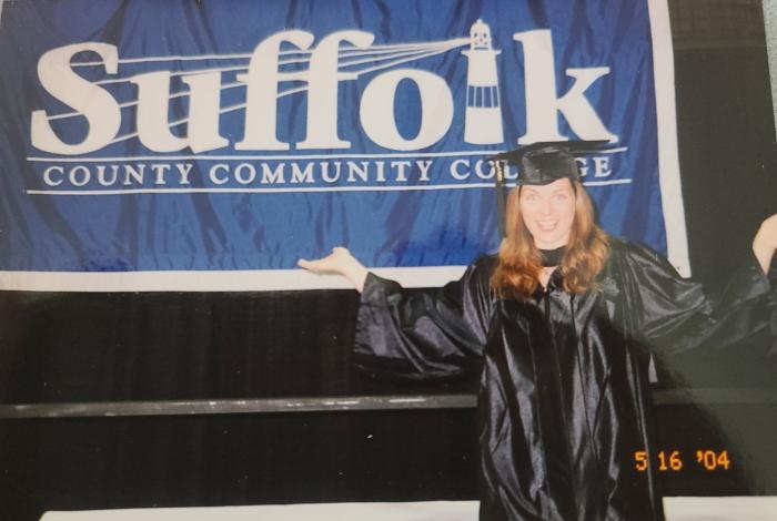christine standing in front of suffolk sign with cap and gown