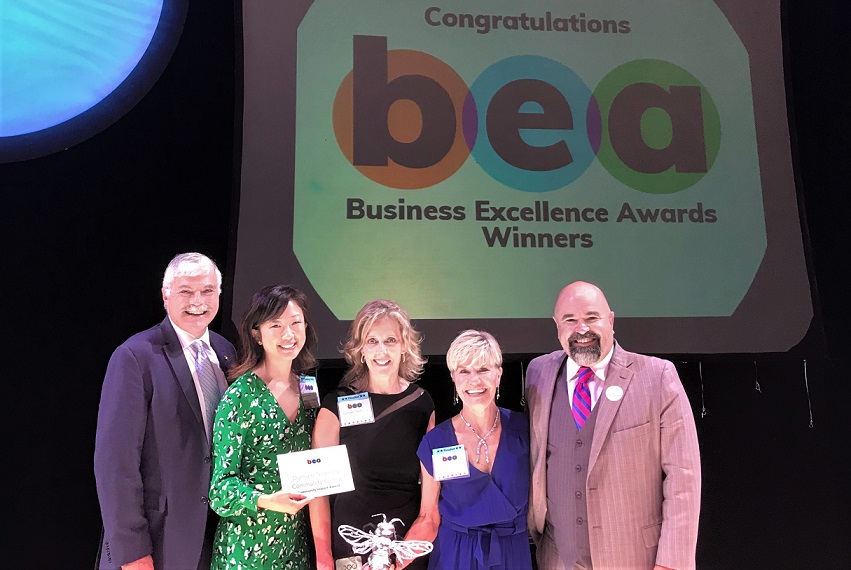 five people smiling on stage in front of a powerpoint presentation screen