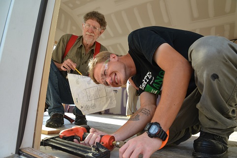 student leaning over using nail gun and another student looking over shoulder