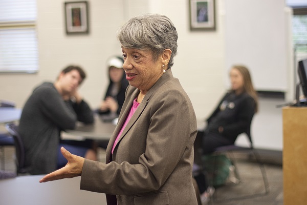 dr. darden speaking in front of room, three students in background sitting at table