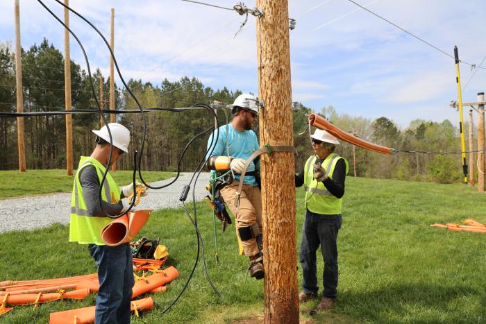 three line technicians standing by wooden pole