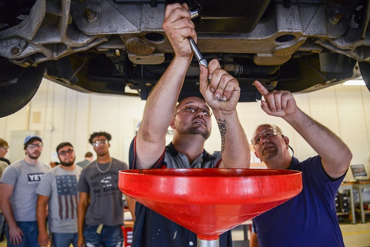 student and instructor under car changing oil while other students watch them