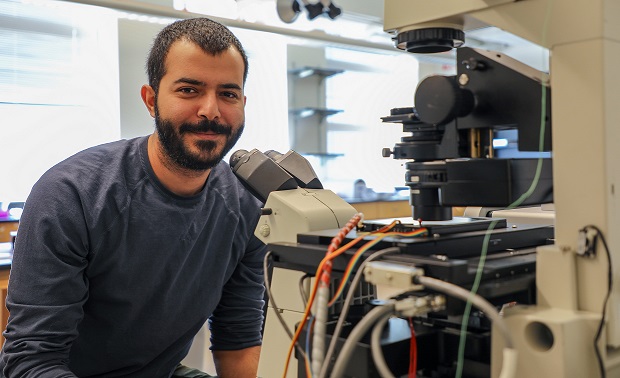 Parsa sits in front of microscope and smiles at camera