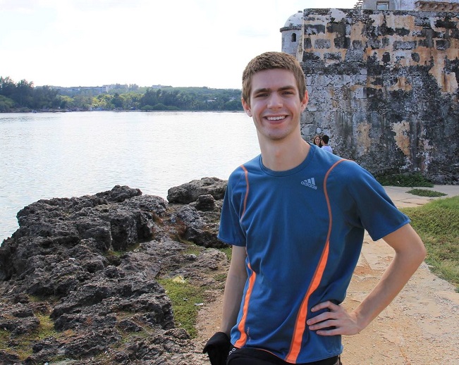 will smiling at camera with water on one side and stone building on other side in background