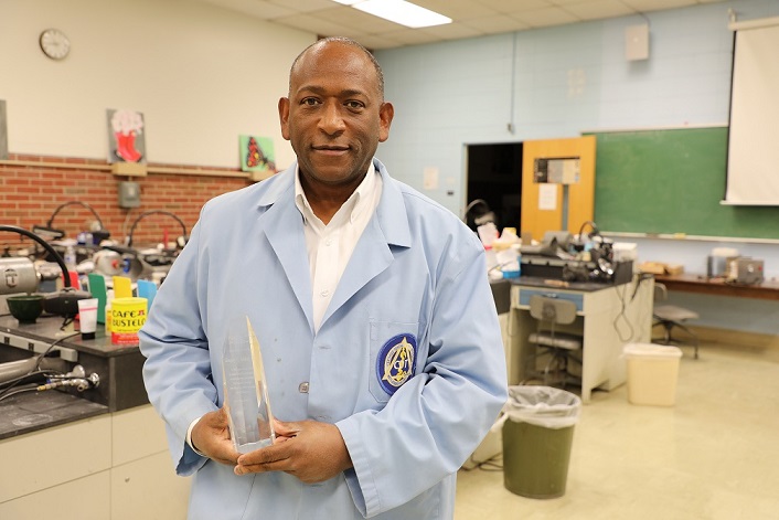 greg standing in dental lab with blue coat holding award