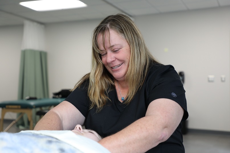 student smiling as they give massage to another student laying on massage bed