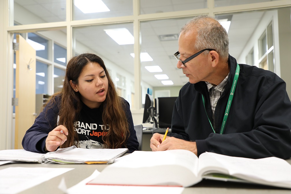 student and tutor sit at table talking 
