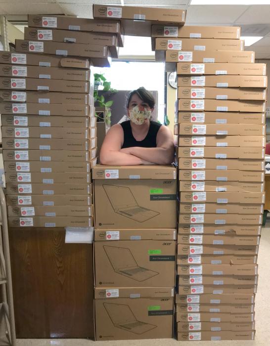 person stands in between a high stack of laptops in boxes