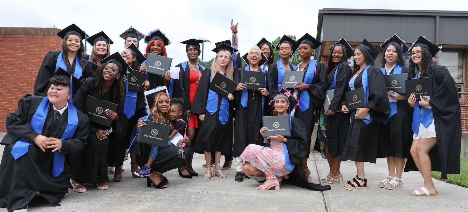 Graduates pose for a photo wearing their cap and gown and holding up their degree