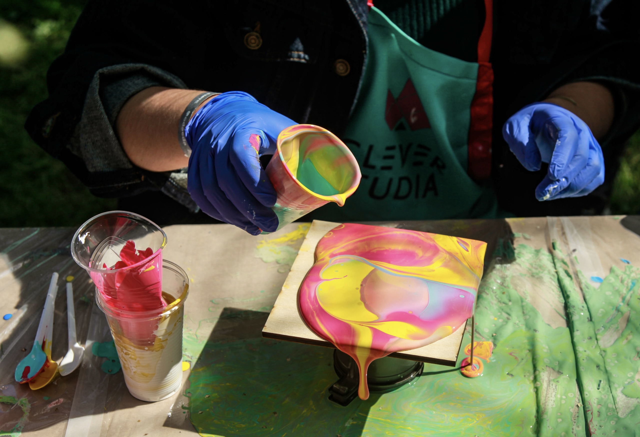 Multi-colored acrylic paint pouring from a cup onto a square canvas