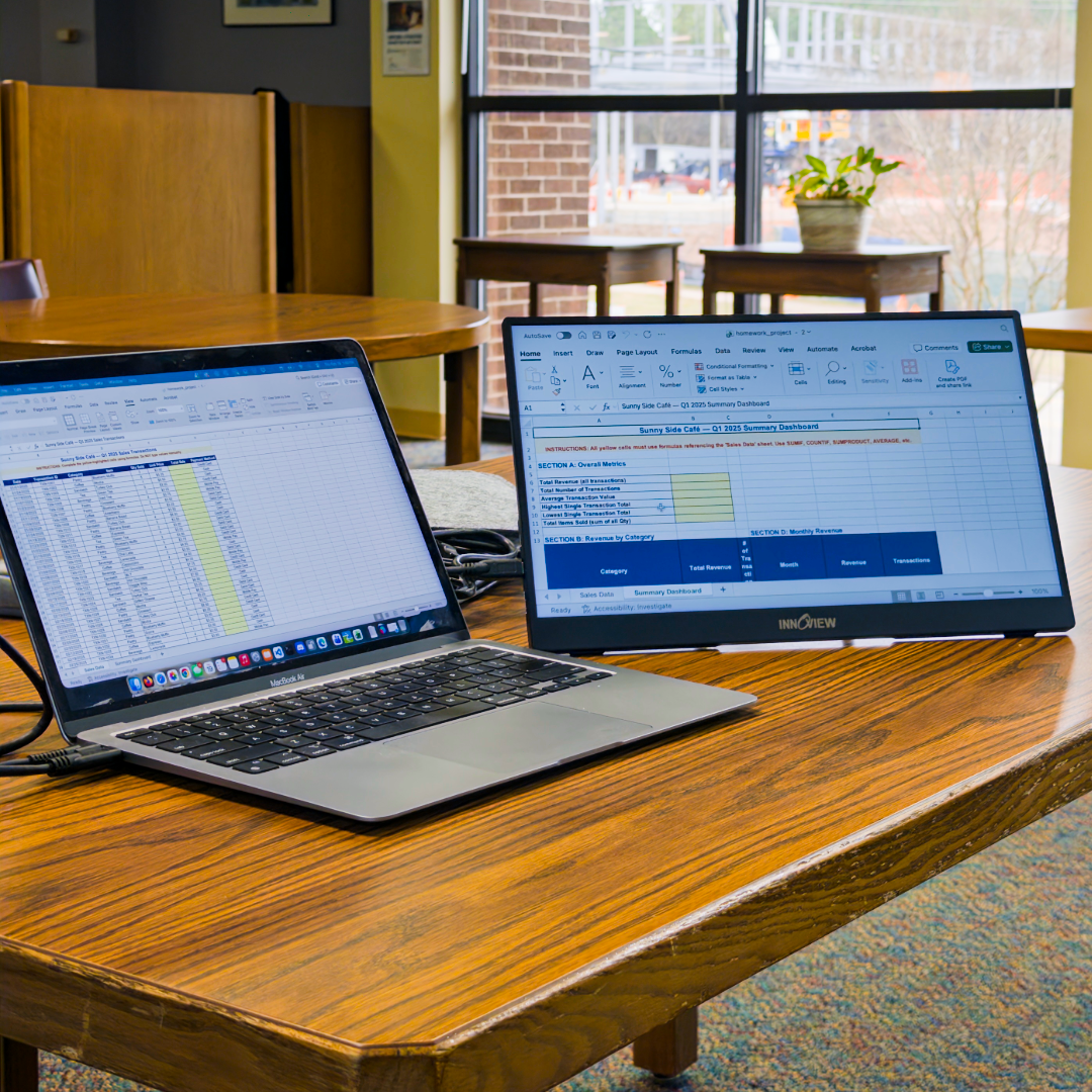 A laptop next to a portable monitor on a wooden table in the library