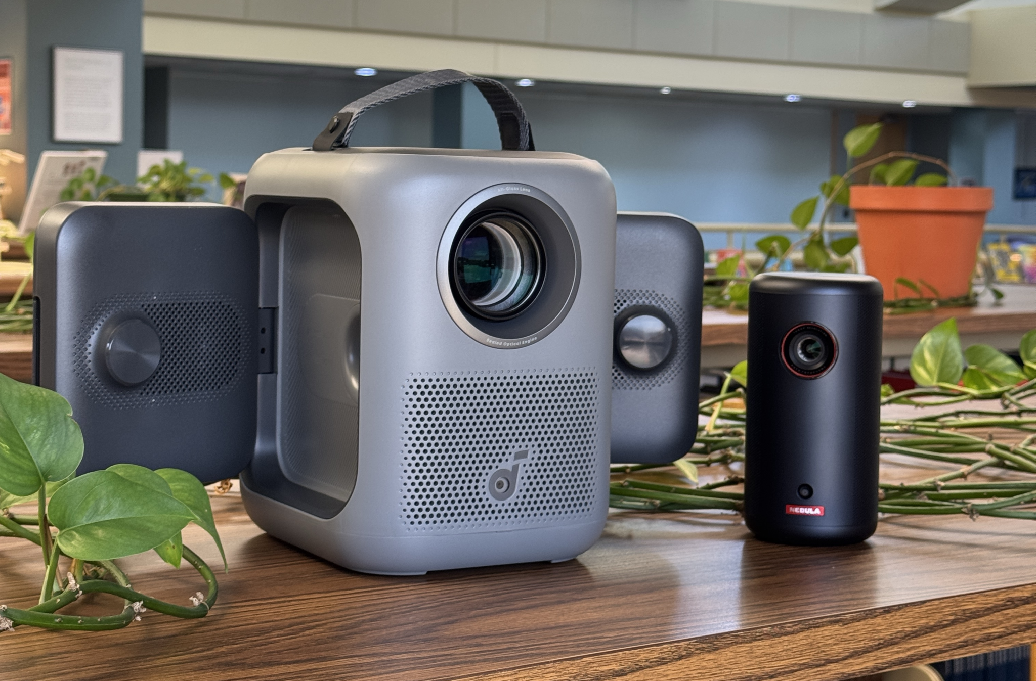 A compact capsule projector beside a larger projector with fold-out side speakers.